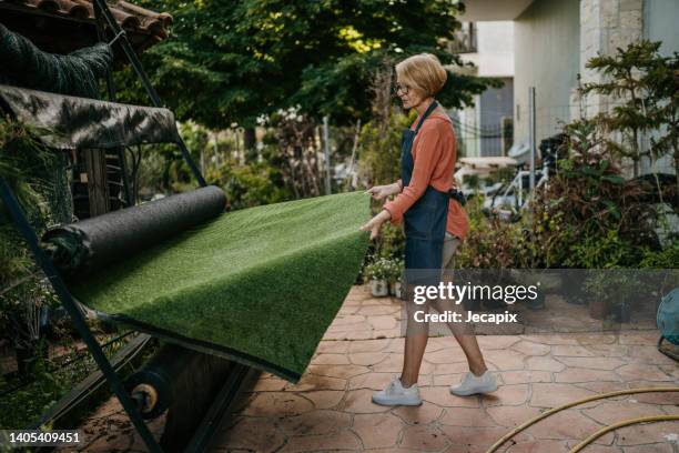 woman rolling out artificial grass carpet - artificial turf stock pictures, royalty-free photos & images