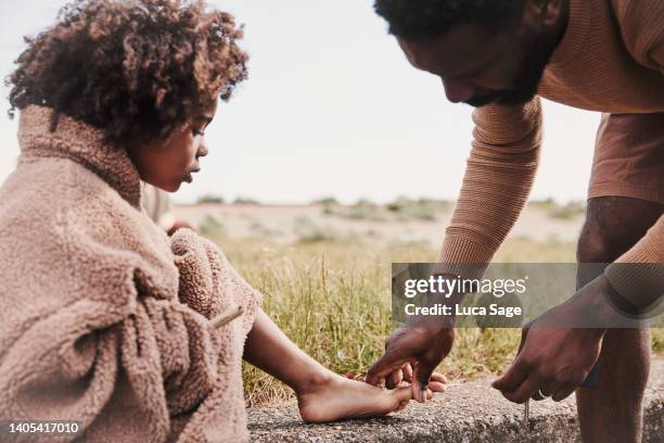 young boy in fathers jumper, being helped by his father during a road trip to the beach with his family. - beach goers stock pictures, royalty-free photos & images