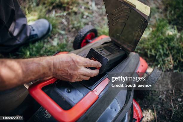 senior man testing battery in electric cordless lawn mower - grasmaaier stockfoto's en -beelden