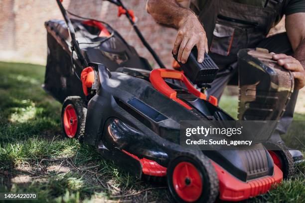 senior man putting battery into electric cordless lawn mower - gräsklippare bildbanksfoton och bilder