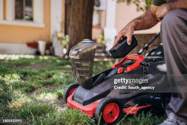 senior man putting battery into electric cordless lawn mower - lawn mower stock pictures, royalty-free photos & images