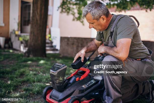 senior man putting battery into electric cordless lawn mower - mower stock pictures, royalty-free photos & images