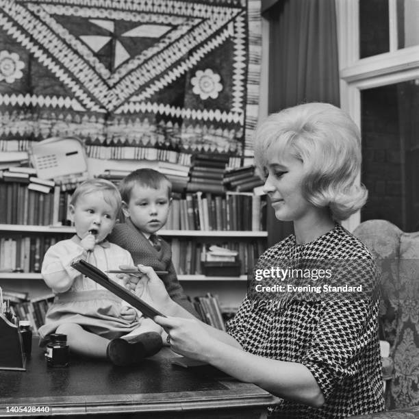 British socialite and actress Elizabeth Rees-Williams wearing a dogtooth check outfit with her sons, Jared Harris and Damian Harris, with bookcases...