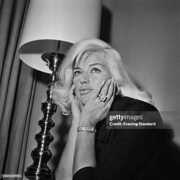 British actress and singer Diana Dors , her chin resting in her hands, a standard lamp in the background, at the Carlton Tower Hotel in...