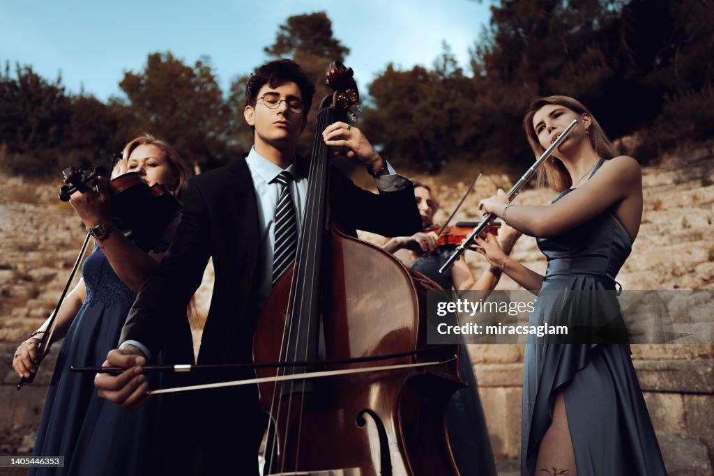 Three musicians in blue dress and one musician in black suit in ancient theater.