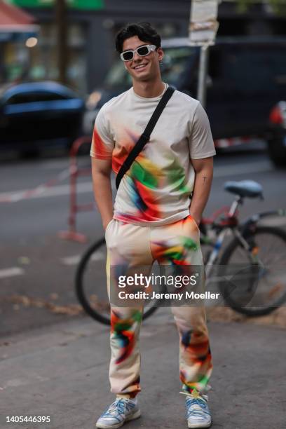 Jacob Rott seen wearing a white Prada sunglasses, a colorful batik t-shirt, matching colorful batik jogger pants, a black crossbody bag and white...