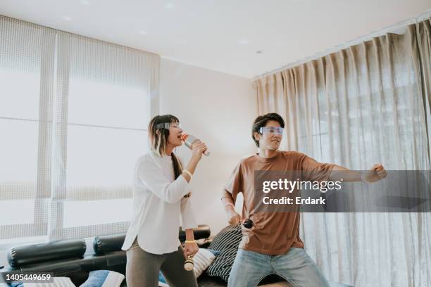 asian couple singing karaoke time and dancing in living room during weekend. - couple dancing at home stockfoto's en -beelden