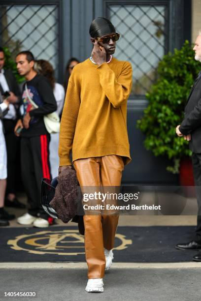 Guest wears a black scarf, brown sunglasses from Versace, a blue and pink pearls necklace, a yellow mustard wool pullover, brown shiny leather...