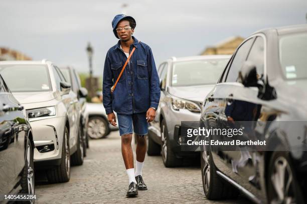 Guest wears a navy blue denim bob, glasses, earrings, a white ribbed tank-top, a navy blue denim oversized shirt jacket, a camel shiny leather...