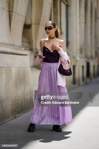 Guest wears futurist sunglasses, gold earrings, a large gold necklace, a gold chain pendant necklace, a dark purple satin V-neck tank-top, a pale...