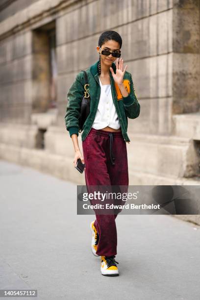 Guest wears black sunglasses from Balenciaga, a gold necklace, a white shoulder-off t-shirt, a white ribbed pattern buttoned cardigan, burgundy large...
