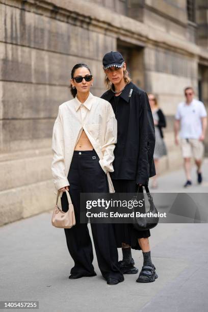 Guest wears black sunglasses from Ray Ban, silver earrings, a white latte oversized shirt, a beige nylon Reedition 2000 handbag from Prada, silver...