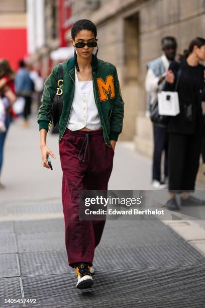 Guest wears black sunglasses from Balenciaga, a gold necklace, a white shoulder-off t-shirt, a white ribbed pattern buttoned cardigan, burgundy large...