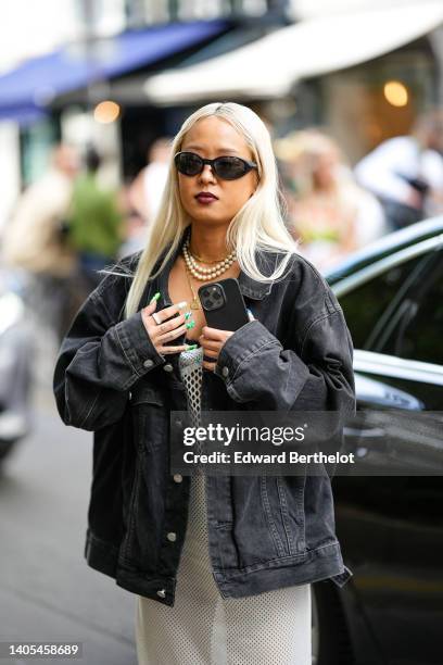 Guest wears black sunglasses, a white pearls necklace, a gold chain necklaces, a black denim oversized jacket, a white mesh long dress, rings,...