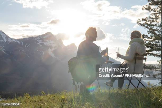 mature couple enjoy a glass of champagne, at mountain viewpoint - escapismo foto e immagini stock