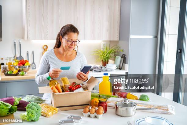 woman with mobile phone and credit card paying groceries - debit cards credit cards accepted stock pictures, royalty-free photos & images