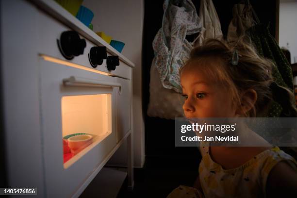 retrato de una niña pequeña jugando en la cocina del bebé y usando el horno para hornear cupcakes. - cupcakes girls fotografías e imágenes de stock