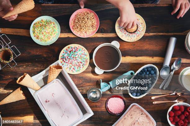 little girls preparing ice cream in cone with various toppings, fruits, and candy sprinklers - ice cream sundae stock pictures, royalty-free photos & images