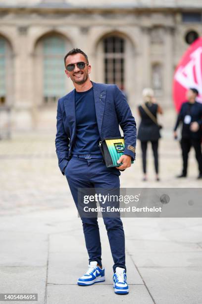 Guest wears black sunglasses from Louis Vuitton, a navy blue t-shirt, a navy blue embossed LV monogram pattern blazer jacket from Louis Vuitton,...