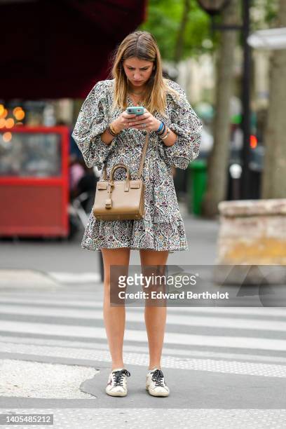 Guest wears a white with burgundy / green / burgundy flower print pattern puffy long sleeves / ruffled short dress, a beige shiny leather Sac Du Jour...