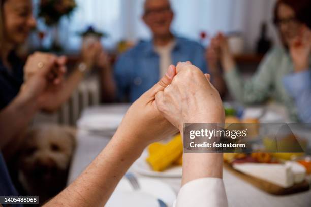 close up shot of senior woman and her son holding hands and praying at the dining table - thanksgiving dog stockfoto's en -beelden