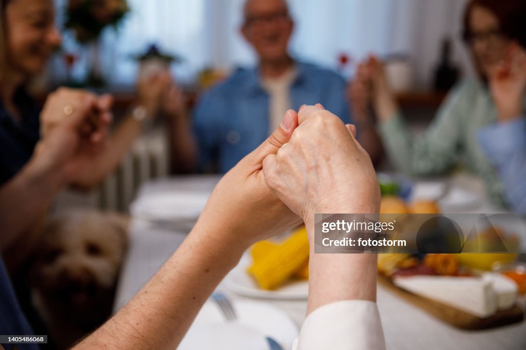 Close up shot of senior woman and her son holding hands and praying at the dining table