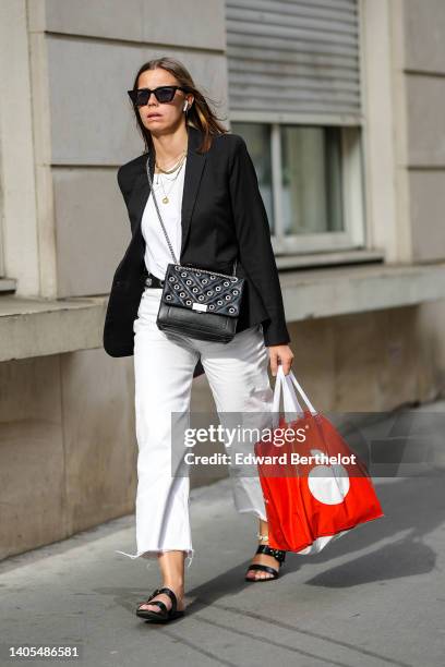Guest wears black sunglasses, silver earrings, gold chain necklaces, a white t-shirt, a black blazer jacket, a black shiny leather nailed / studded...