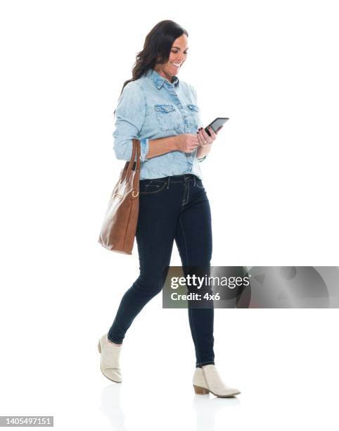 mulheres jovens caucasianas andando em frente ao fundo branco vestindo jeans e segurando bolsa e usando telefone inteligente - smart casual - fotografias e filmes do acervo