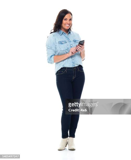 mulher caucasiana em pé na frente de fundo branco vestindo jeans e usando telefone inteligente - smart casual - fotografias e filmes do acervo