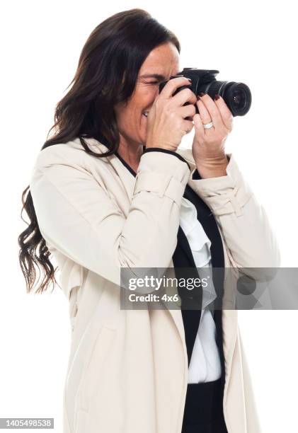 caucasian young women photographer standing in front of white background wearing trench coat and holding camera - camera white background stock pictures, royalty-free photos & images