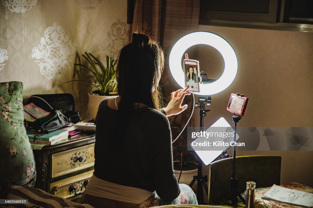 Asian female influencer filming content using phone in a bedroom