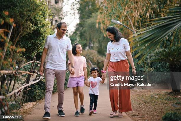 family with two daughters walking together in the garden - indian family portrait stockfoto's en -beelden