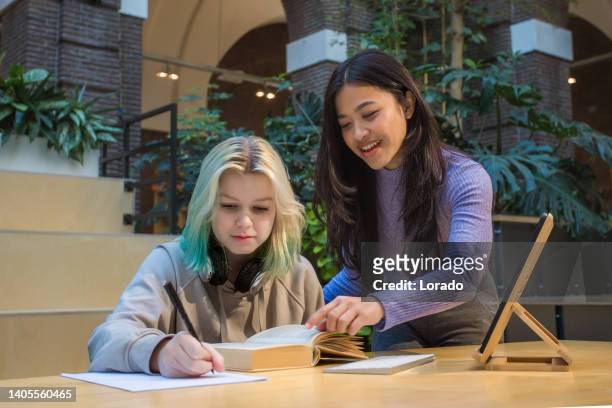 beautiful female child student studying in a public library with a tutor - international student day stock pictures, royalty-free photos & images