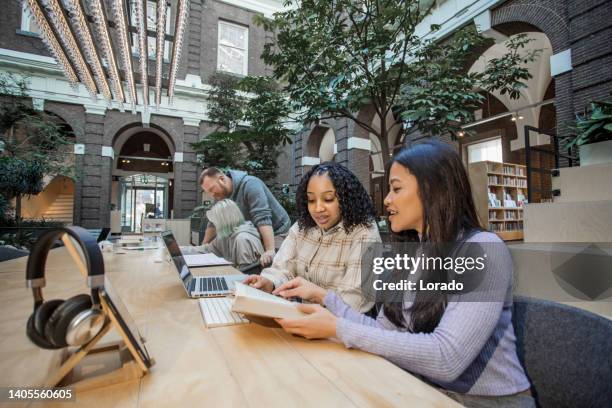 schöne gemischtrassige studentin, die in einer öffentlichen bibliothek mit einem tutor studiert - mixed age range stock-fotos und bilder