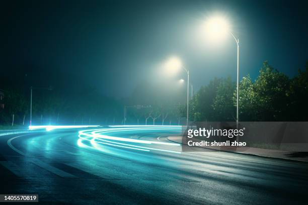 low angle of a spooky road, going into the distance with street lights, glowing on a moody foggy night - vehicle light fotografías e imágenes de stock