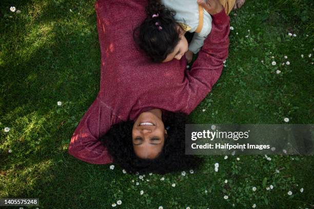 portrait of multiracial woman lying in grass with her daughter and enjoying summer time. - happy family grass stock-fotos und bilder