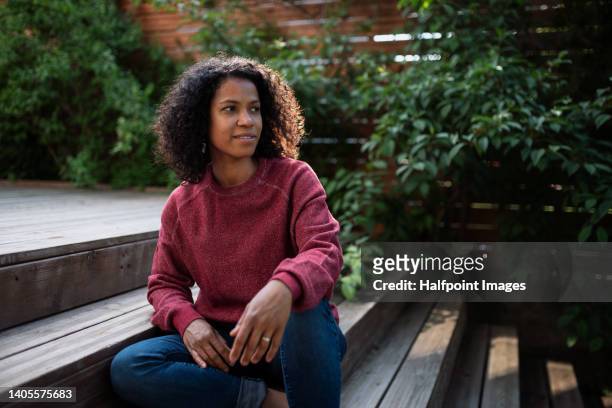 multiracial woman sitting in garden staircase, enjoying summer time. - 40 year old stock pictures, royalty-free photos & images