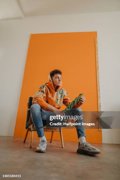 young adult caucasian man sitting and posing in front of orange background. - male fashion model stock pictures, royalty-free photos & images