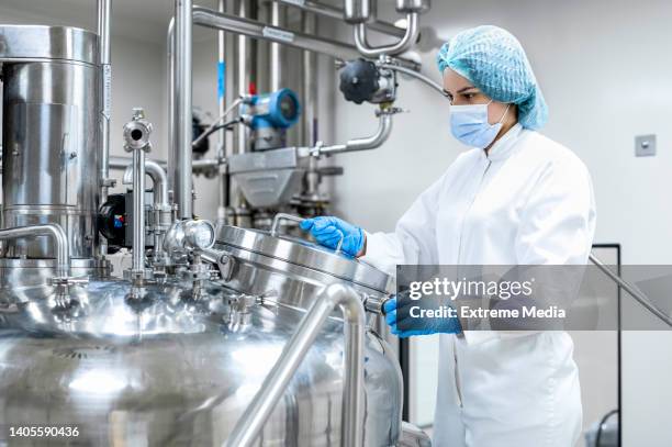 mujer totalmente equipada vista sosteniendo una máquina en un laboratorio de la industria farmacéutica - industria-farmaceutica fotografías e imágenes de stock