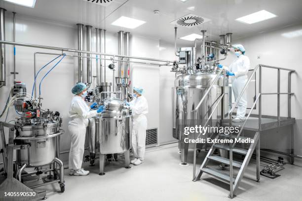 three fully equipped employees in protective workwear seen in a pharmaceutical laboratory - sala limpa imagens e fotografias de stock