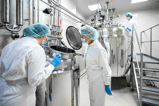 Three fully equipped employees in protective workwear seen in a pharmaceutical laboratory