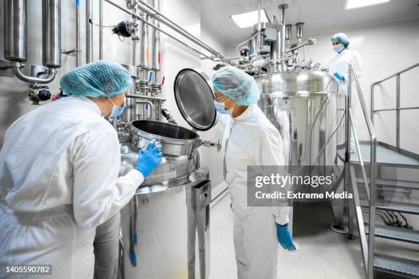 three fully equipped employees in protective workwear seen in a pharmaceutical laboratory - cleanroom stock pictures, royalty-free photos & images