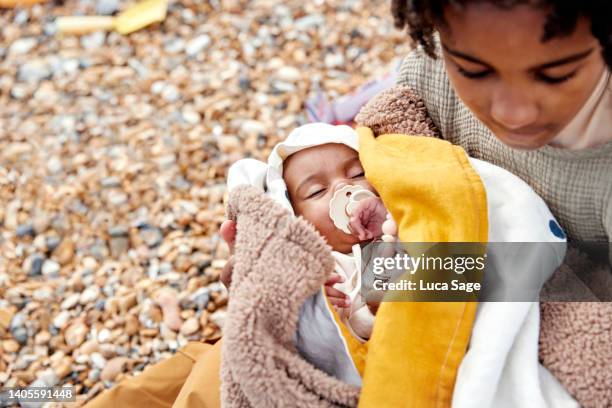 brother lovingly holding his baby sister on the beach - rock baby sleep stock pictures, royalty-free photos & images