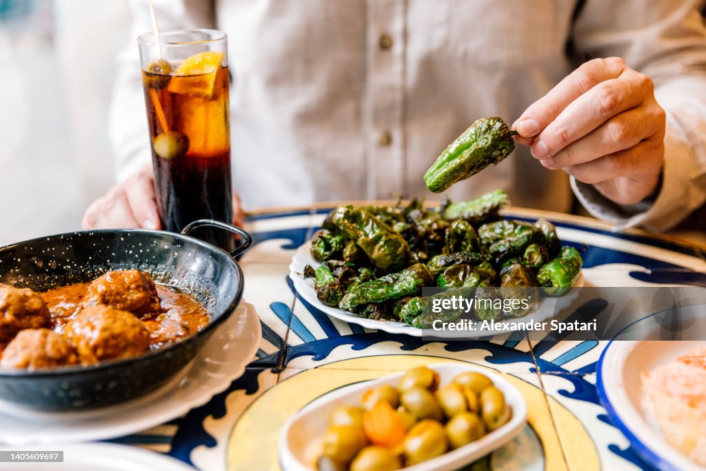 Man eating fried green bell peppers (Pimientos de Padrón) with vermouth in tapas bar, Barcelona, Spain