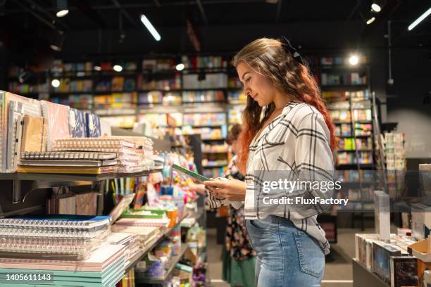 joven caucásica en la librería en busca de un libro - librería fotografías e imágenes de stock