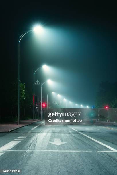 low angle of a spooky road, going into the distance with street lights, glowing on a moody foggy night - hdri background stock pictures, royalty-free photos & images