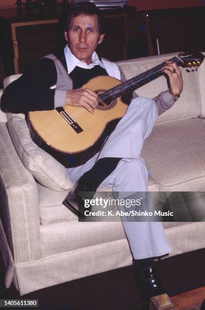 Chet Atkins plays acoustic guitar on a sofa At RCA, Nashville, TN, US, 18th January 1978.