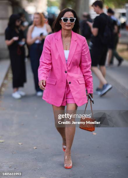 Guest seen wearing white sunglasses from Celine, a silver pendant necklace, a white top, a pink oversize blazer, matching pink shorts, a red leather...