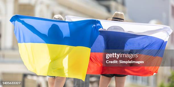 a back view of two friends with the flags of ukraine and the russia somewhere in a ukrainian city. - ryssland bildbanksfoton och bilder