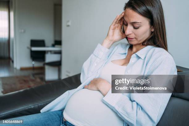 sad pregnant woman sitting on the sofa with her hand at belly. - morning sickness stockfoto's en -beelden